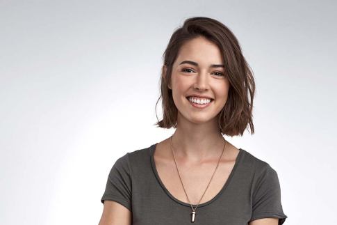 Young woman smiles warmly, standing with arms folded and wearing a pendant necklace