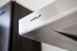 Stainless-steel range hood mounted above a stove in a modern kitchen with blurred dark wood cabinets in the background.