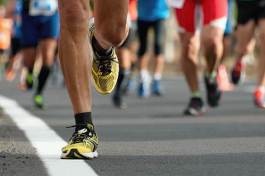 A runner's legs and yellow running shoes propel forward, mid-stride, on a paved road