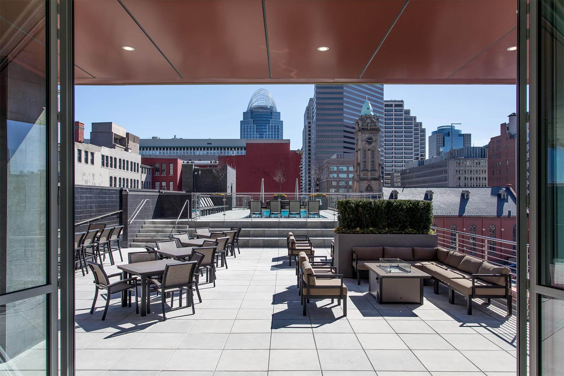 Rooftop terrace overlooking a city skyline with skyscrapers, a clock tower, and pool area under a clear blue sky.