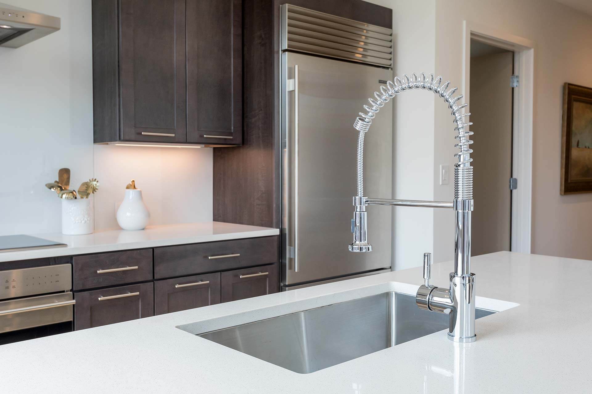 Chrome spring-coil kitchen faucet stands over an empty stainless sink, mounted in a white quartz island