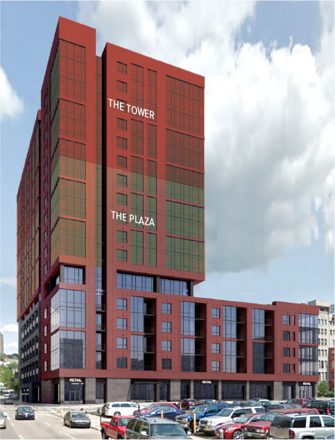 A tall red mixed-use building rises above a low podium beside a parked-car lot under a cloudy sky.